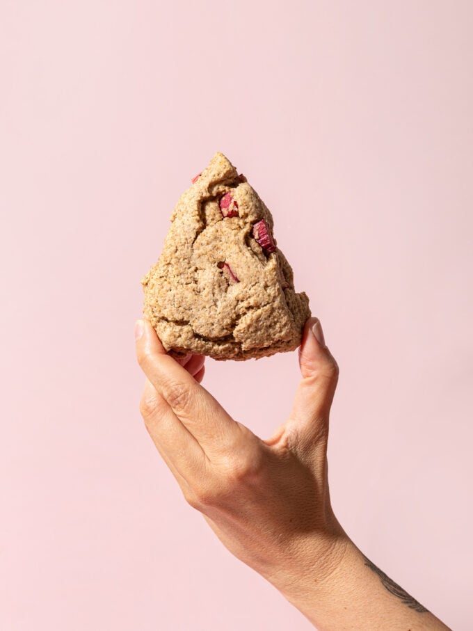 hand holding rhubarb scone in front of pink wall
