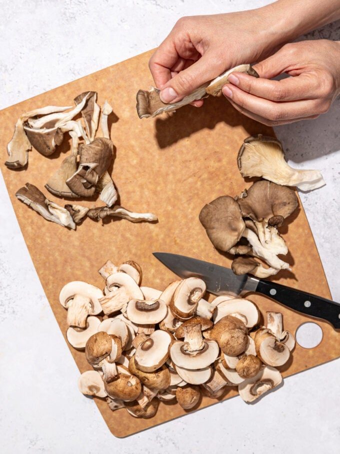 hand tearing oyster mushrooms on wooden cutting board