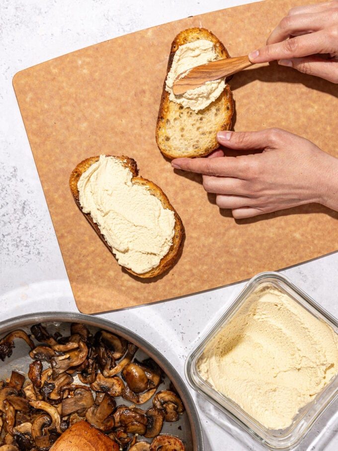 hand spreading tofu ricotta on slices of sourdough toast