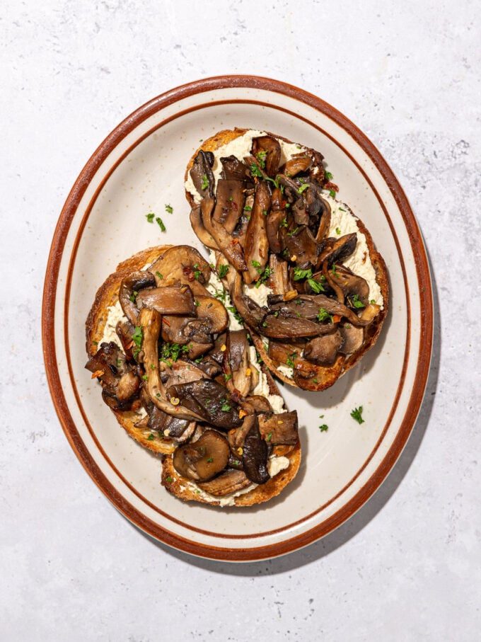 mushrooms on 2 slices of toast on a brown rimmed oblong plate