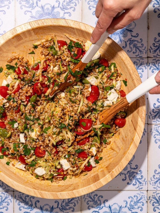 hands tossing a farro vegetable salad in a wooden bowl