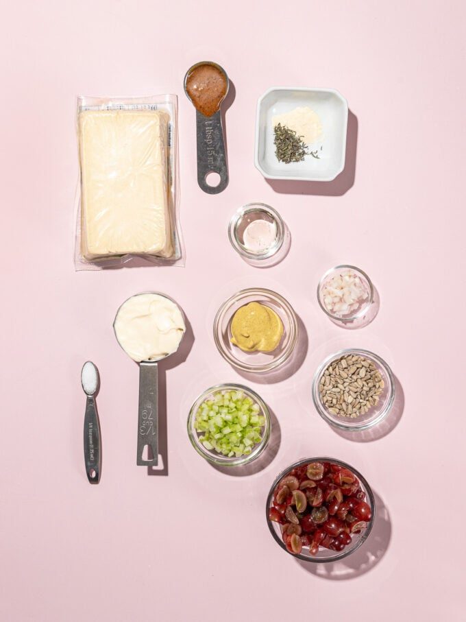 various bowls of spoonfuls of ingredients - red grapes, tofu, mayo, celery, bouillon concentrate - on a pink backdrop