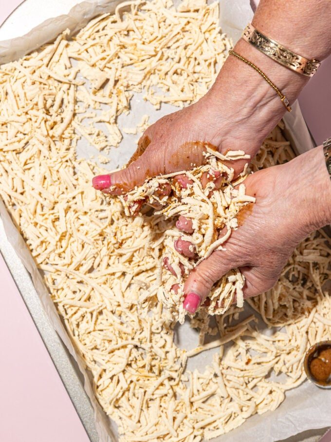 hands massaging shredded tofu with bouillon concentrate over baking sheet