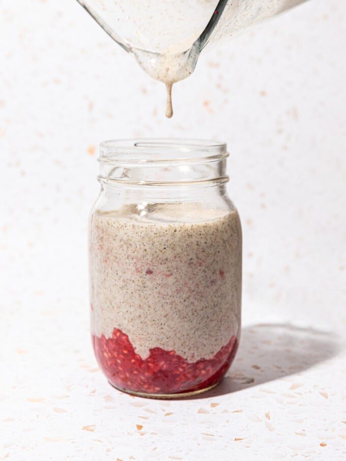 pouring chia pudding into jar of smashed raspberries