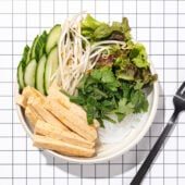 tofu, vermicelli noodles, lettuce and herbs in a white bowl with a black fork laying beside it