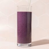tall glass of blueberry beet smoothie with glass straw on a pink tile background