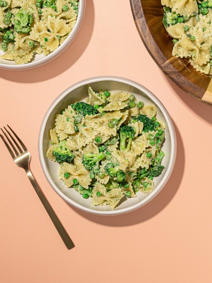 white bowls of broccoli bowtie pasta salad with wooden serving bowl and fork