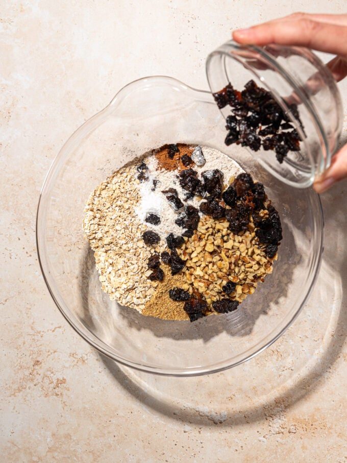 hand adding diced prunes to mixing bowl with cookie ingredients