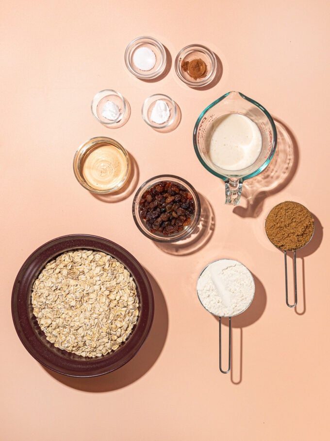 bowls of oatmeal cookie ingredients: rolled oats, soy milk, brown sugar, flour, raisins and cinnamon