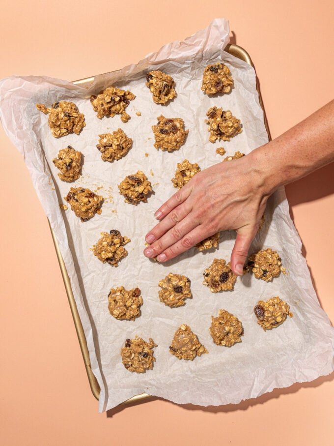 hand pressing down raw oatmeal raisin cookie batter on baking sheet