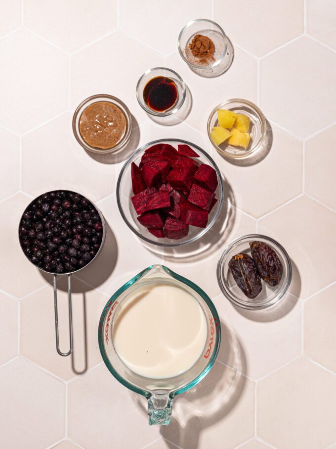 small glass bowls of ingredients: raw chopped beet, blueberries, fresh ginger, dates, almond butter, cinnamon