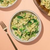 white bowls of broccoli bowtie pasta salad with wooden serving bowl and fork