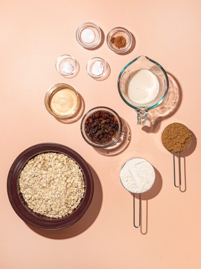 bowls of oatmeal cookie ingredients: rolled oats, soy milk, brown sugar, flour, raisins and cinnamon