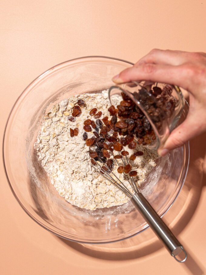 hand pouring raisins into bowl of flour and rolled oats