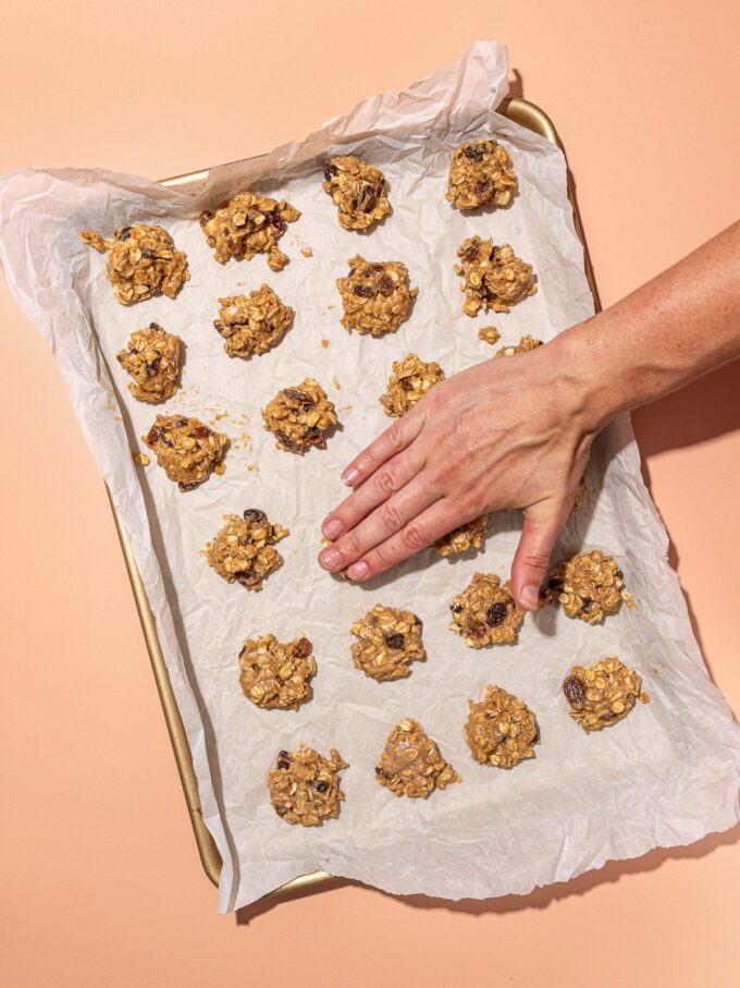 hand pressing down raw oatmeal raisin cookie batter on baking sheet